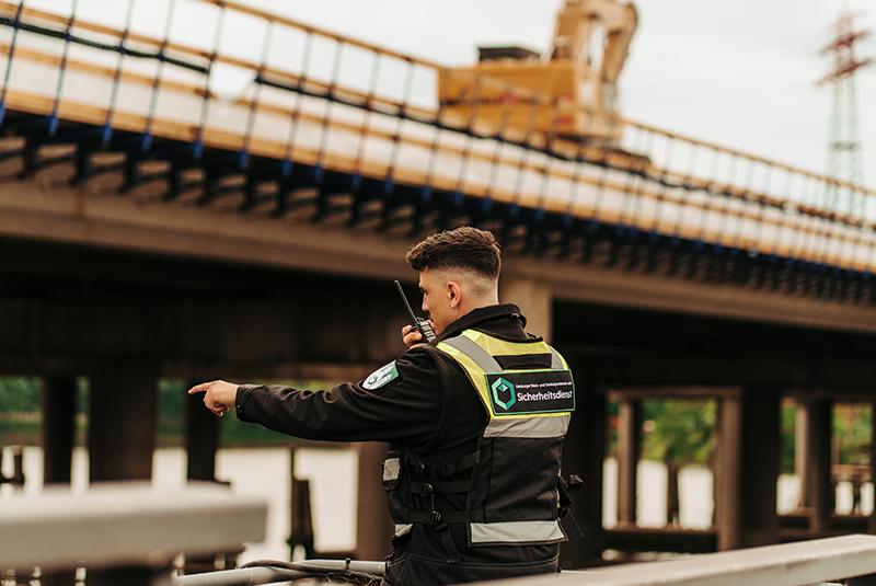 Ein Sicherheitsdienstmitarbeiter zeigt energisch auf etwas unter einer Brücke.